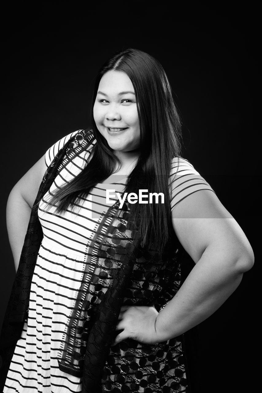 Portrait of smiling woman standing against black background