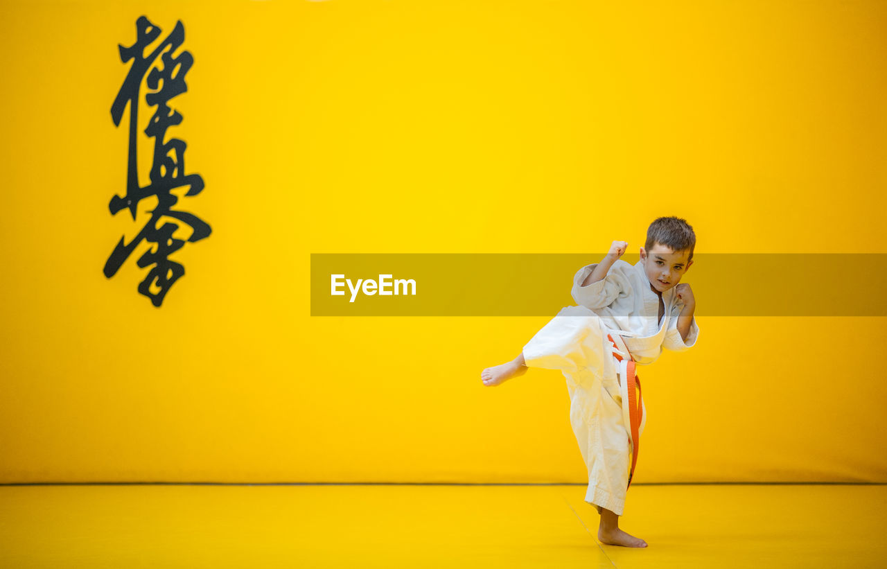 Portrait of cute boy practicing martial arts against yellow wall