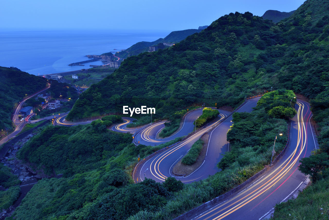 High angle view of light trails on road by mountain against sky