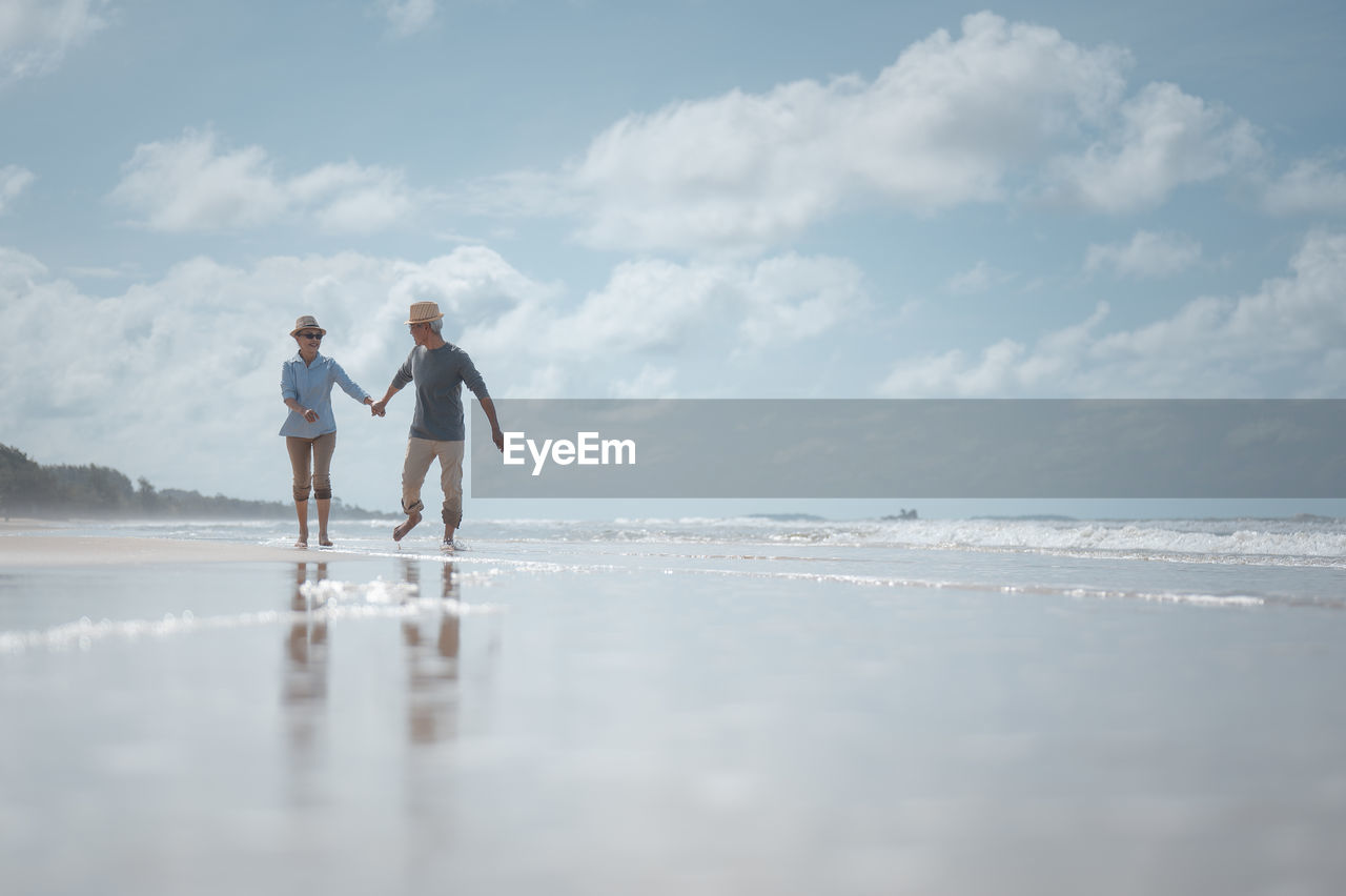 Couple holding hands while walking at beach against sky