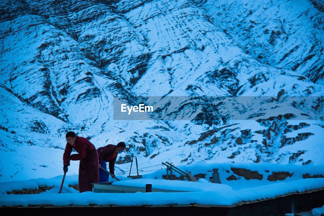 MAN STANDING ON SNOW COVERED MOUNTAINS