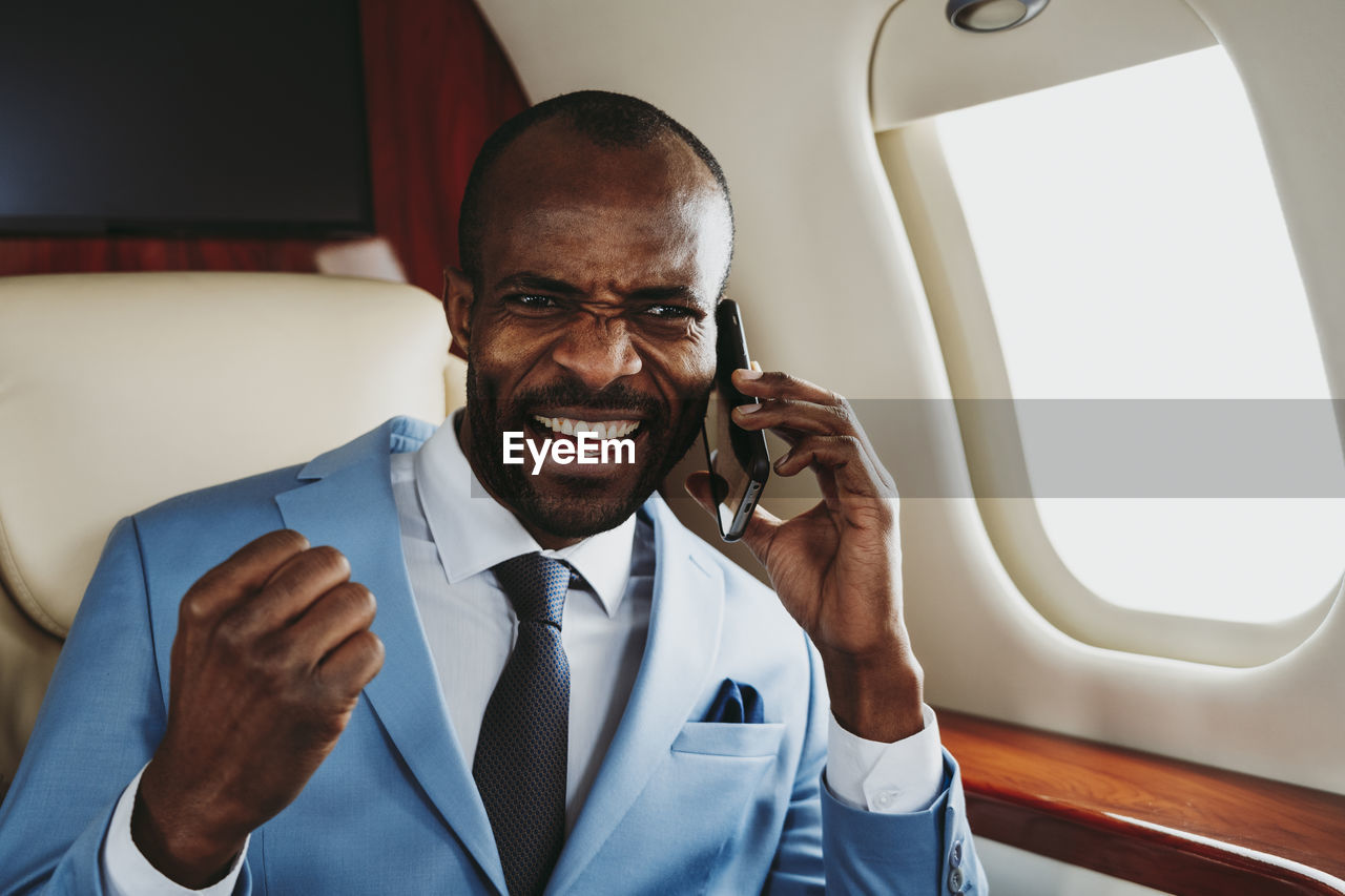 Cheerful businessman talking on smart phone in airplane