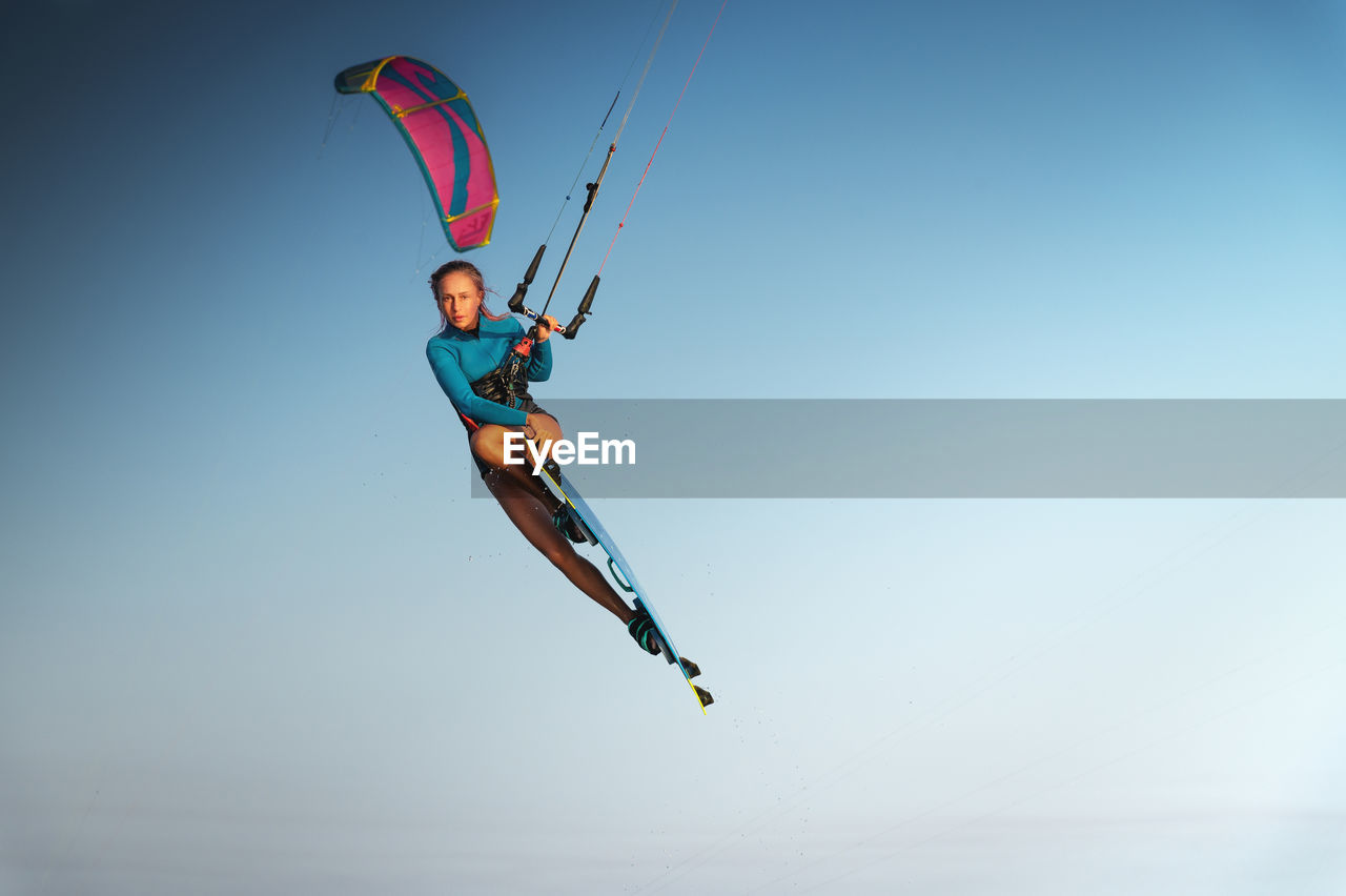 Caucasian woman kitesurfer athlete doing a trick in the air against a blue sky without a cloud