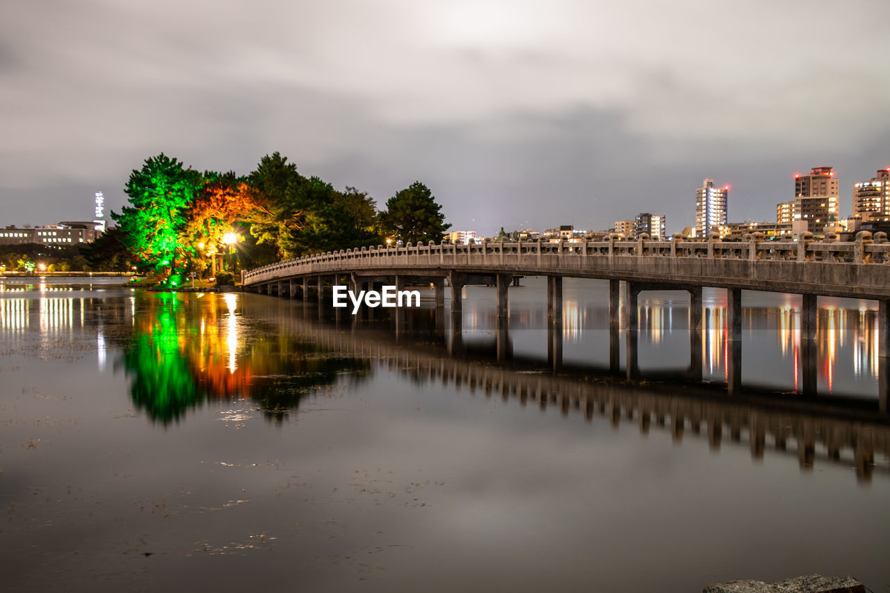 ILLUMINATED BRIDGE OVER RIVER AGAINST SKY AT NIGHT