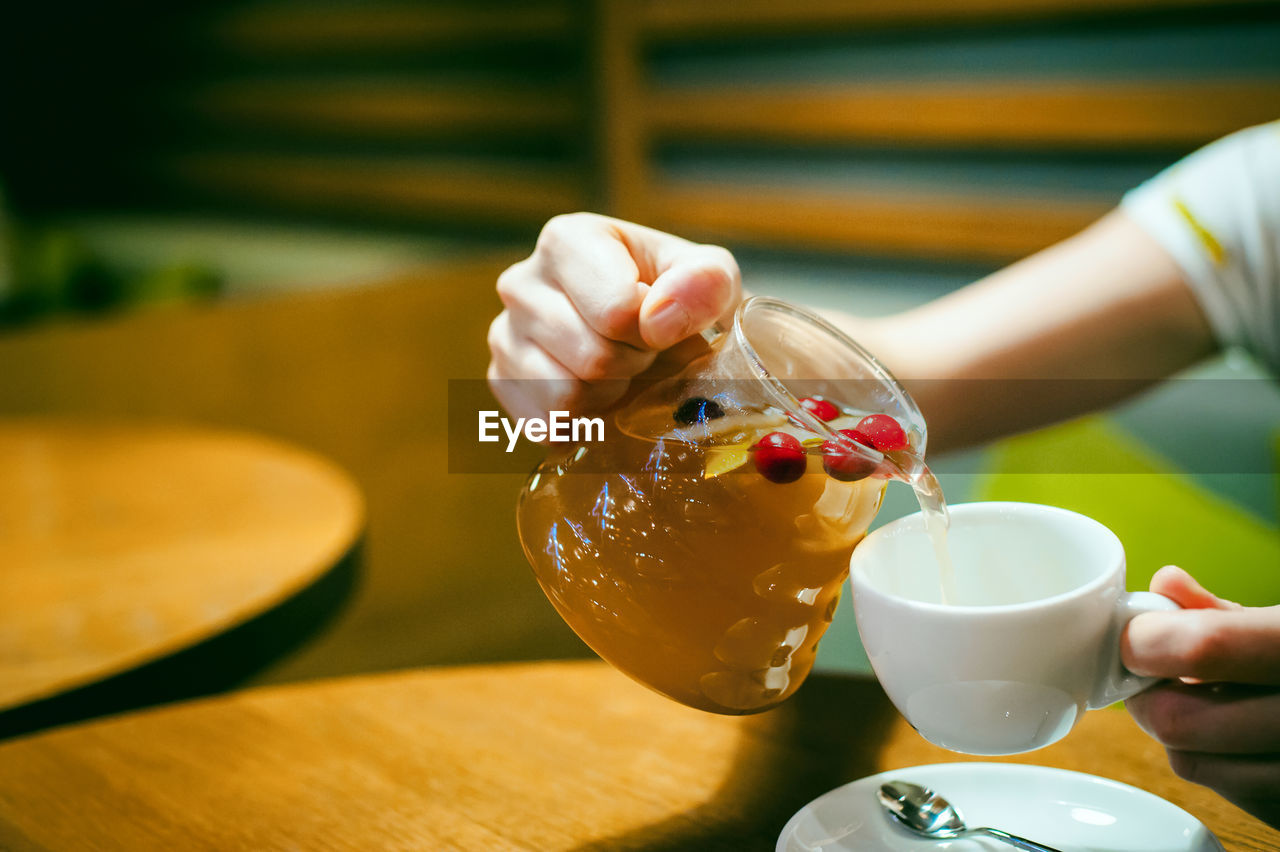 Cropped image of woman pouring drink in coffee cup at restaurant