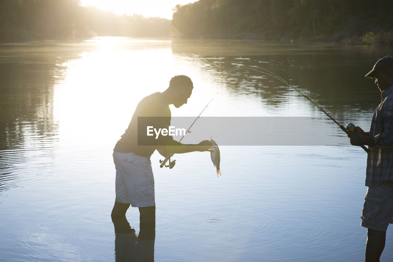 Side view of male friends fishing in lake during sunset