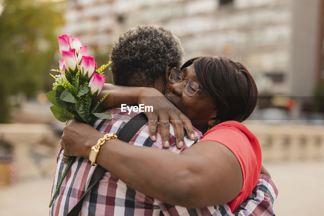 Woman with bunch of flowers embracing man