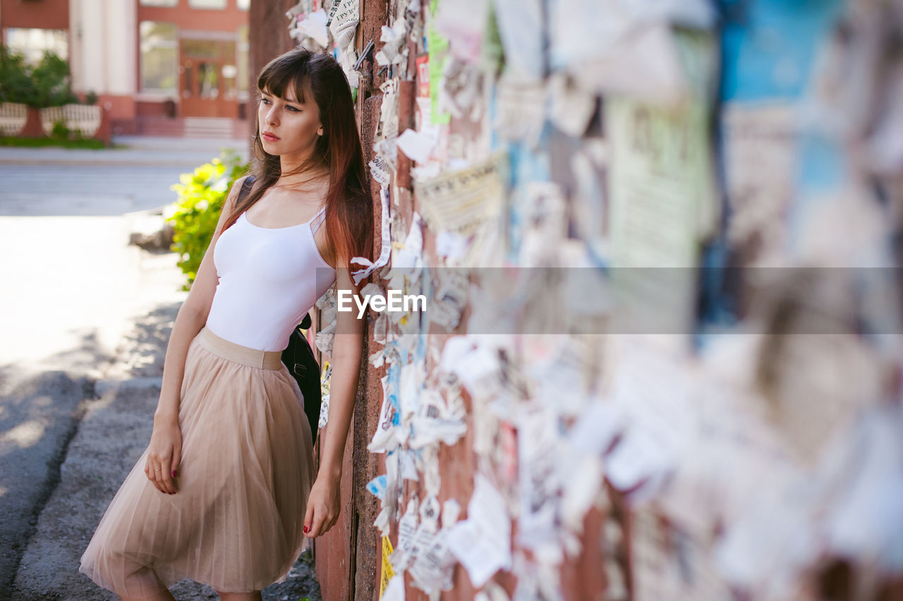 Young woman leaning on wall with torn posters