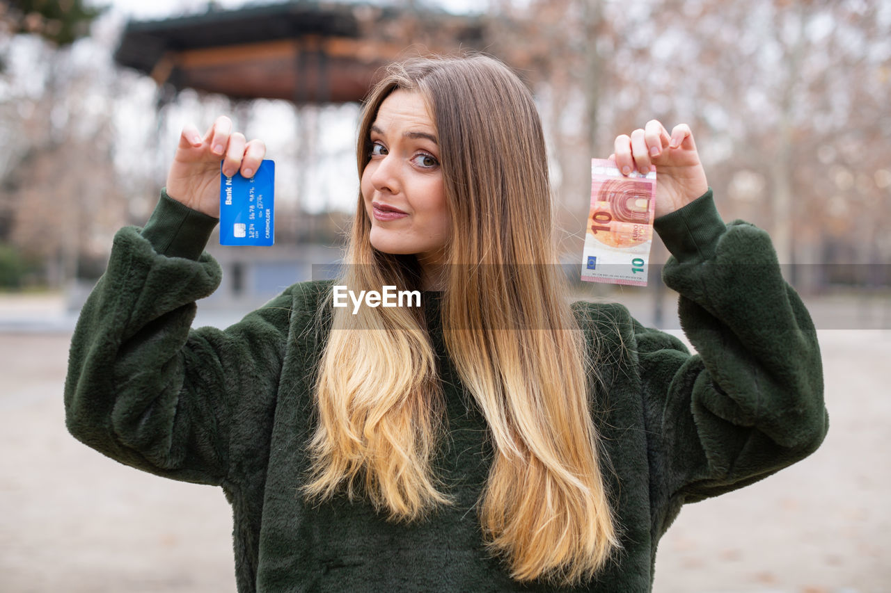 Portrait of woman holding credit card and money while standing outdoors