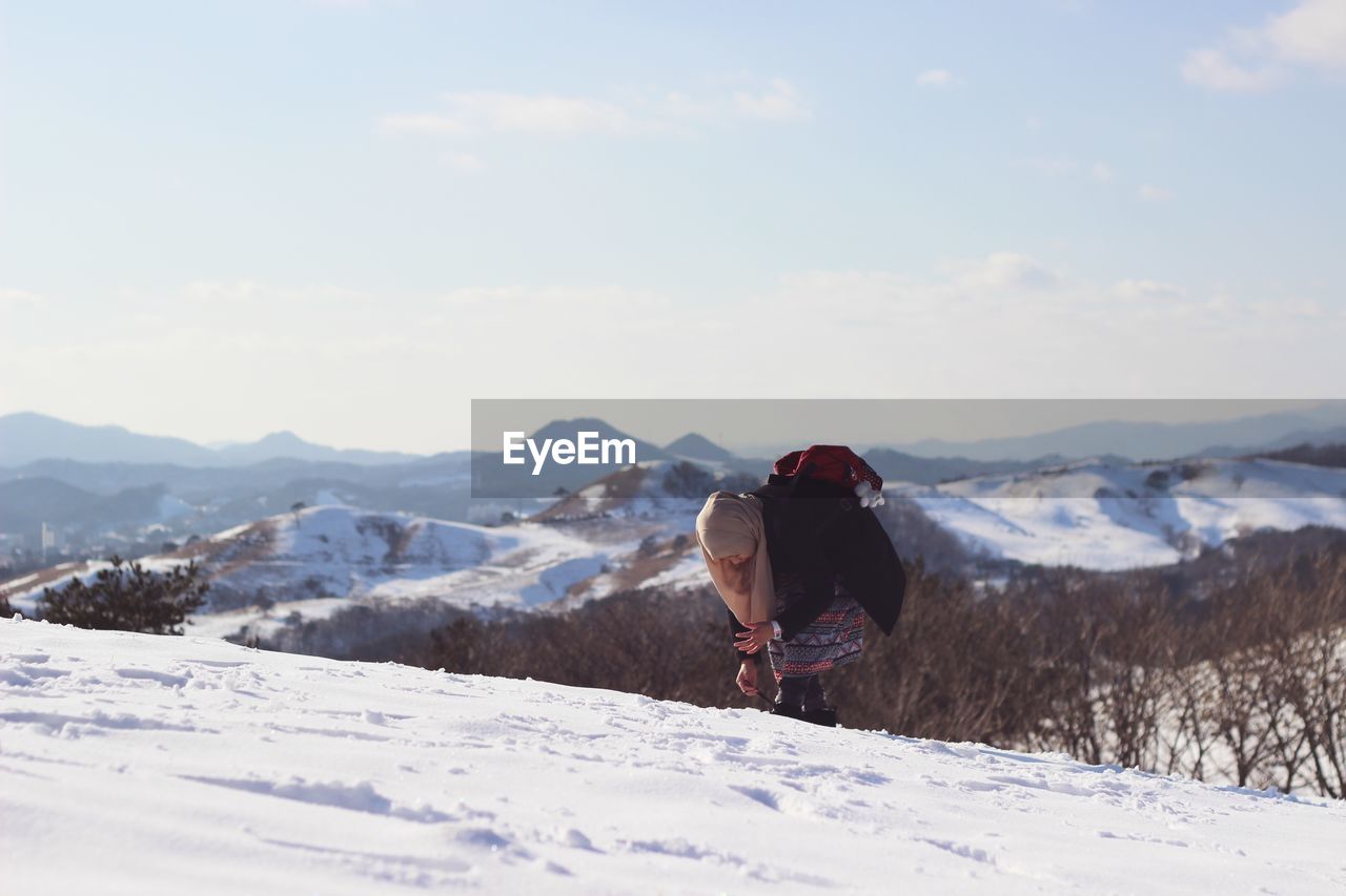 Woman on snowcapped mountain peak against sky