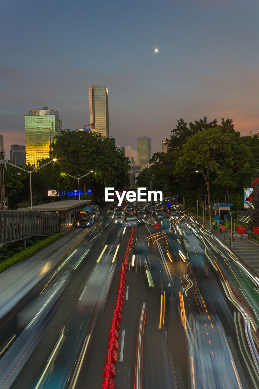 city, architecture, transportation, road, building exterior, highway, built structure, night, street, motion, long exposure, illuminated, traffic, light trail, sky, mode of transportation, cityscape, metropolitan area, motor vehicle, car, city life, evening, city street, speed, lane, infrastructure, street light, building, skyline, nature, office building exterior, moon, skyscraper, overpass, dusk, tail light, travel destinations, high angle view, no people, freeway, urban area, downtown, travel, urban skyline, sign, outdoors, blurred motion, landscape, symbol, on the move, tree, lighting equipment, plant, light, multiple lane highway, headlight, land vehicle, downtown district, the way forward, road marking, residential district, urban road, business finance and industry