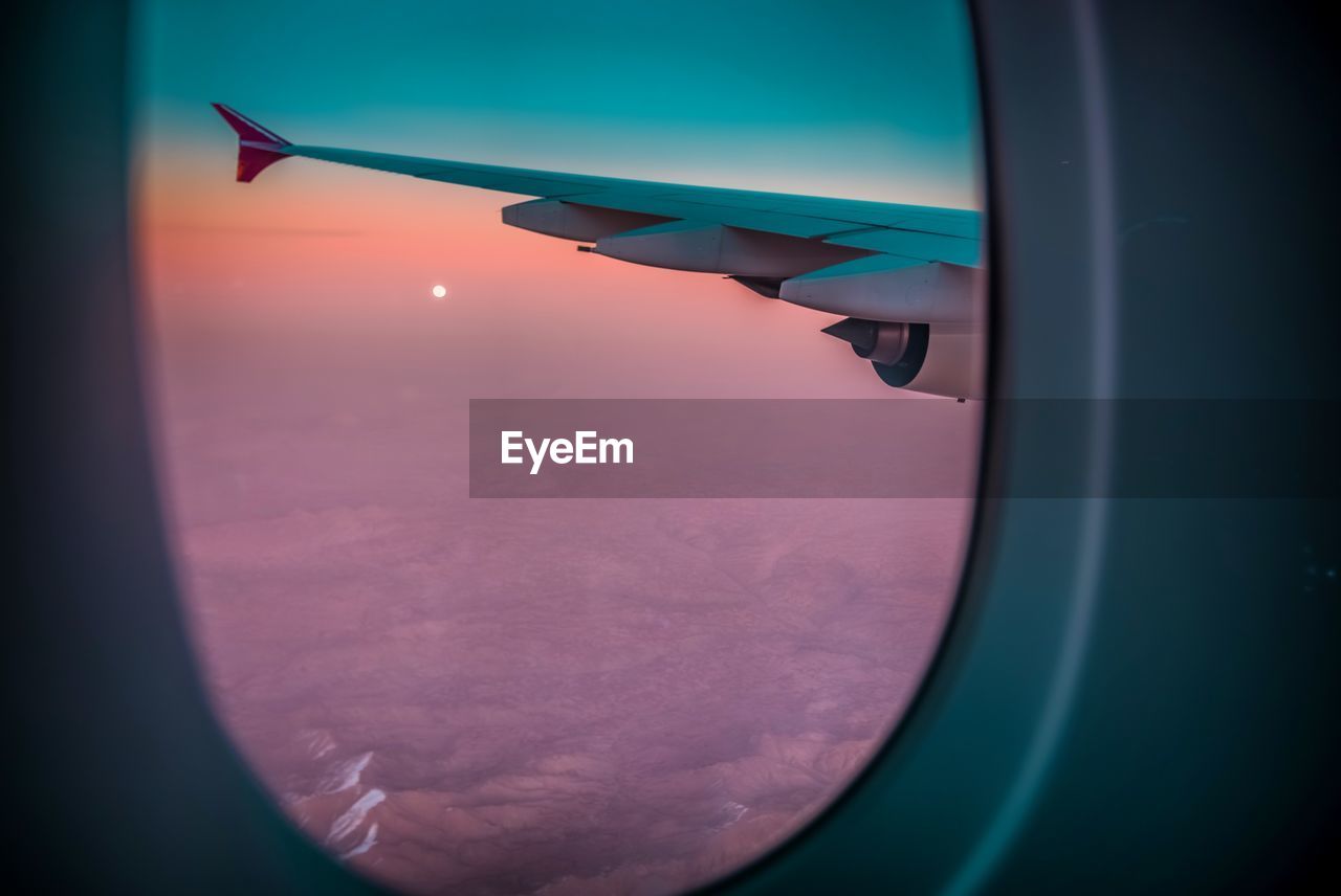 Airplane wing against sky during sunset seen through window