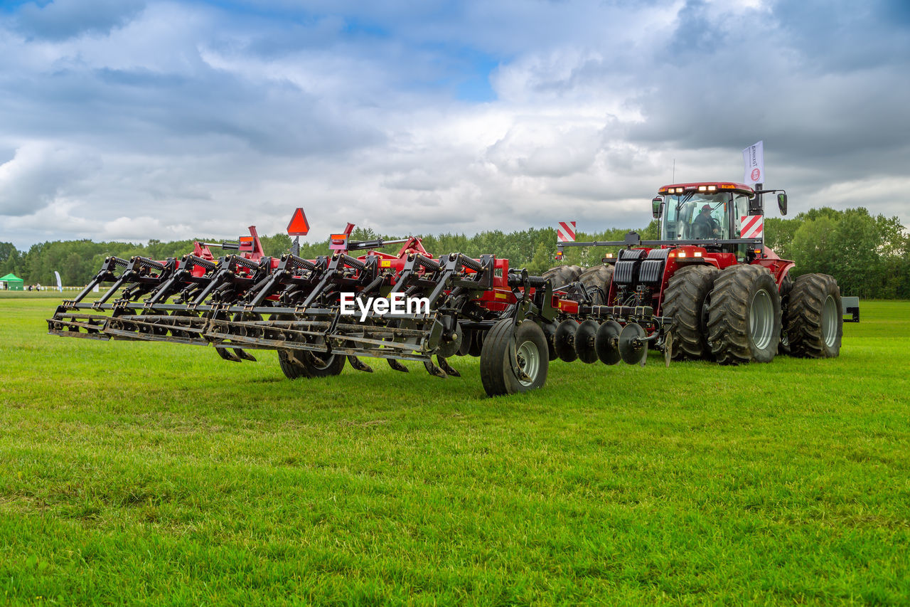 tractor, field, agriculture, agricultural machinery, plant, transportation, sky, nature, agricultural equipment, landscape, rural scene, farm, land, cloud, mode of transportation, grass, vehicle, environment, machinery, land vehicle, plough, day, occupation, green, rural area, harvesting, growth, harvester, outdoors, crop, in a row, wheel