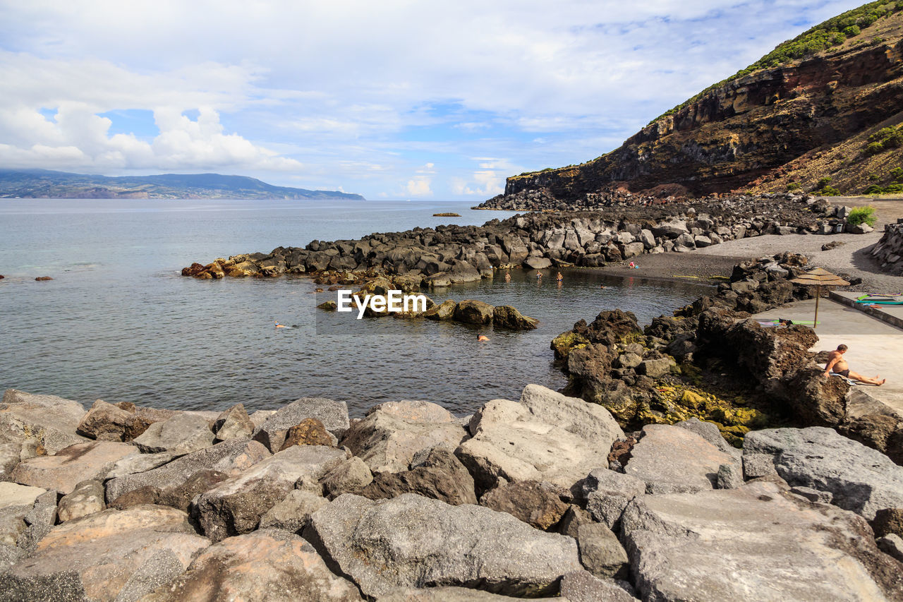 Rocks on shore by sea against sky