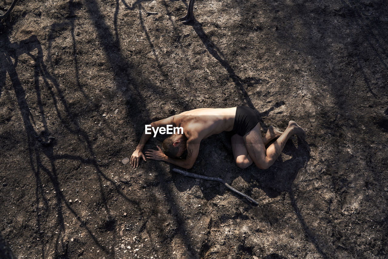 Lonely man lying on burned forest floor