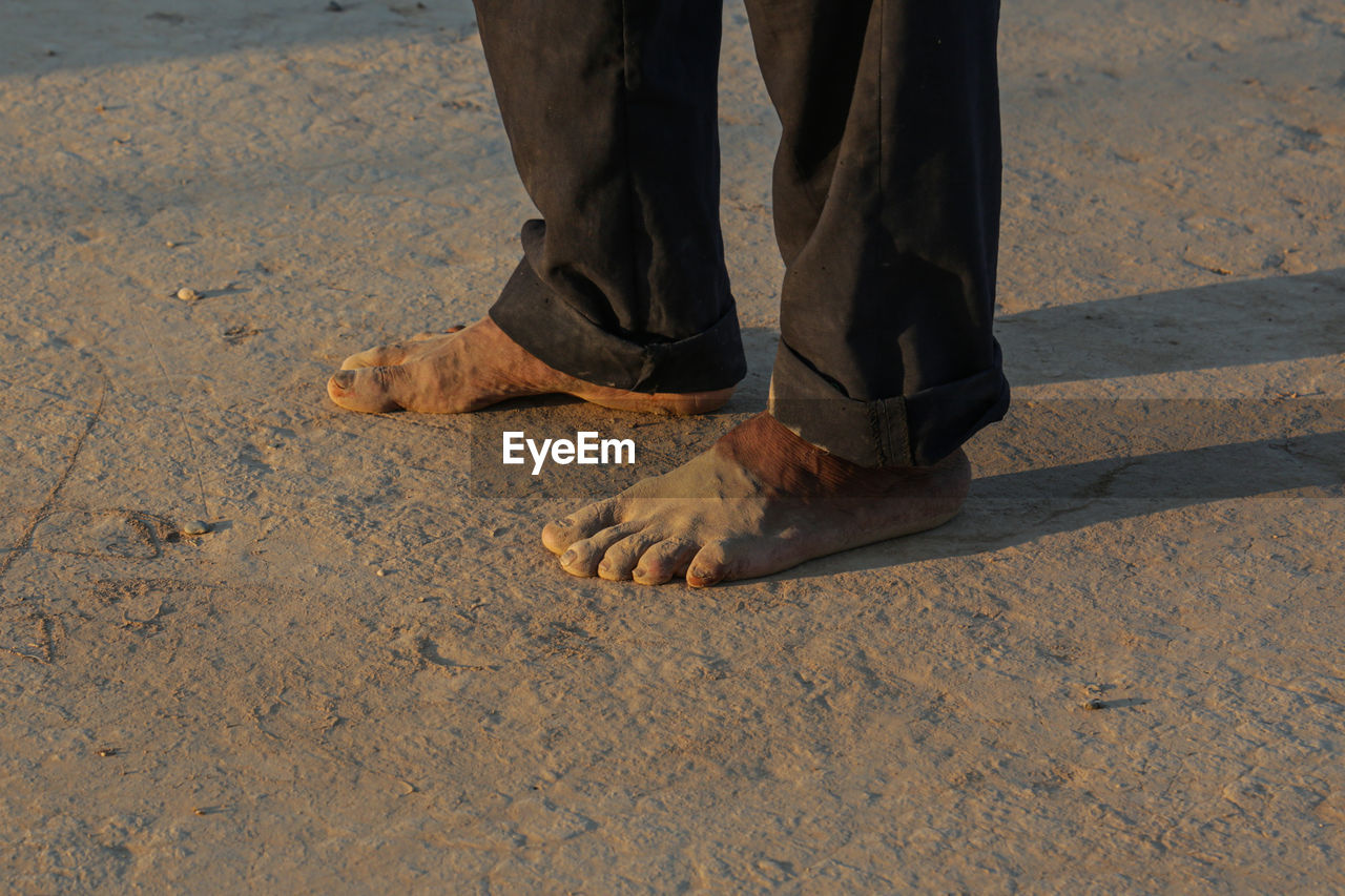 low section, human leg, sand, human limb, limb, one person, land, standing, shoe, men, day, nature, shadow, sunlight, human foot, beach, wood, lifestyles, floor, outdoors, adult, walking, soil, barefoot, leisure activity