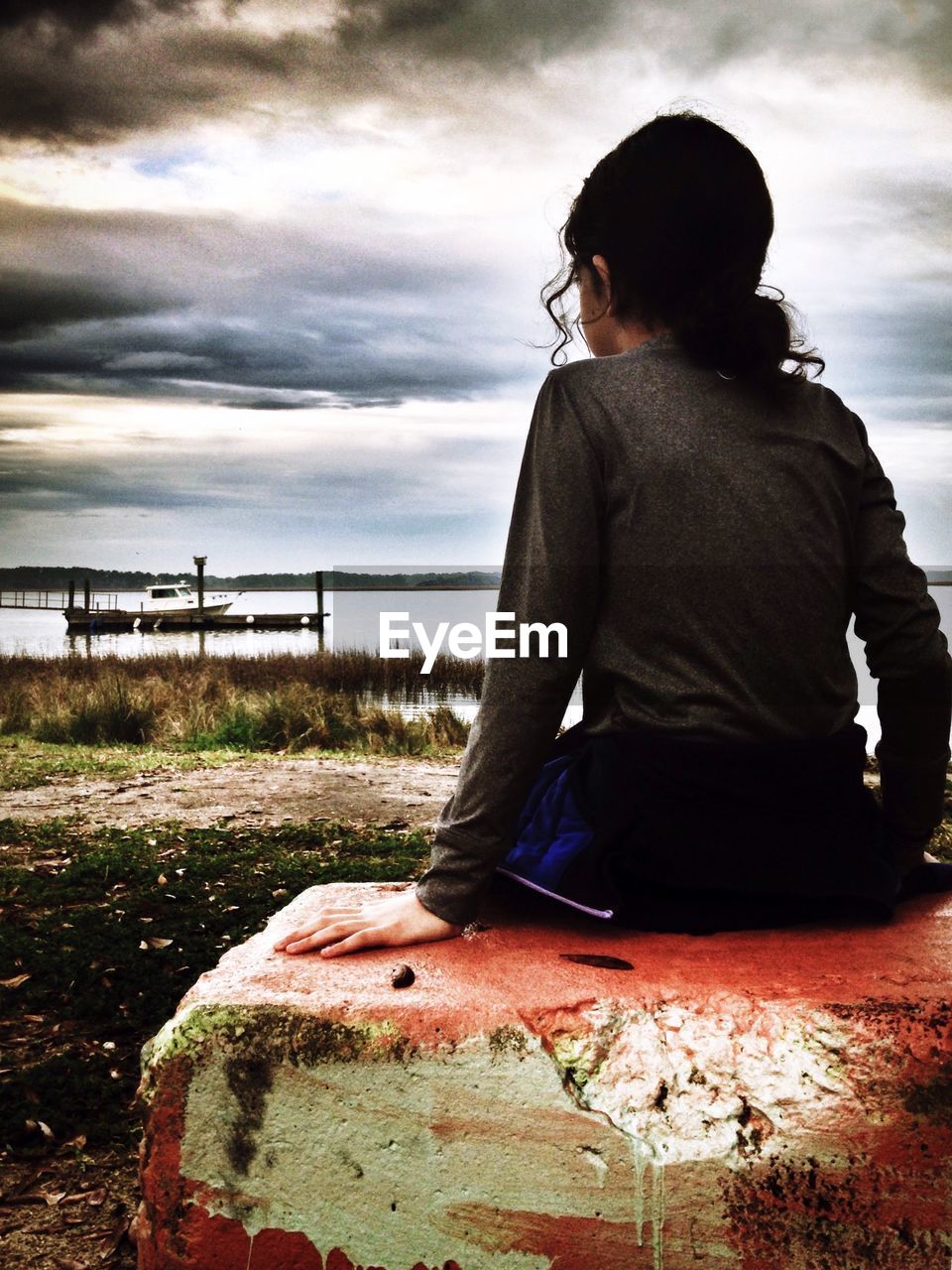 Rear view of girl sitting on rock against sky