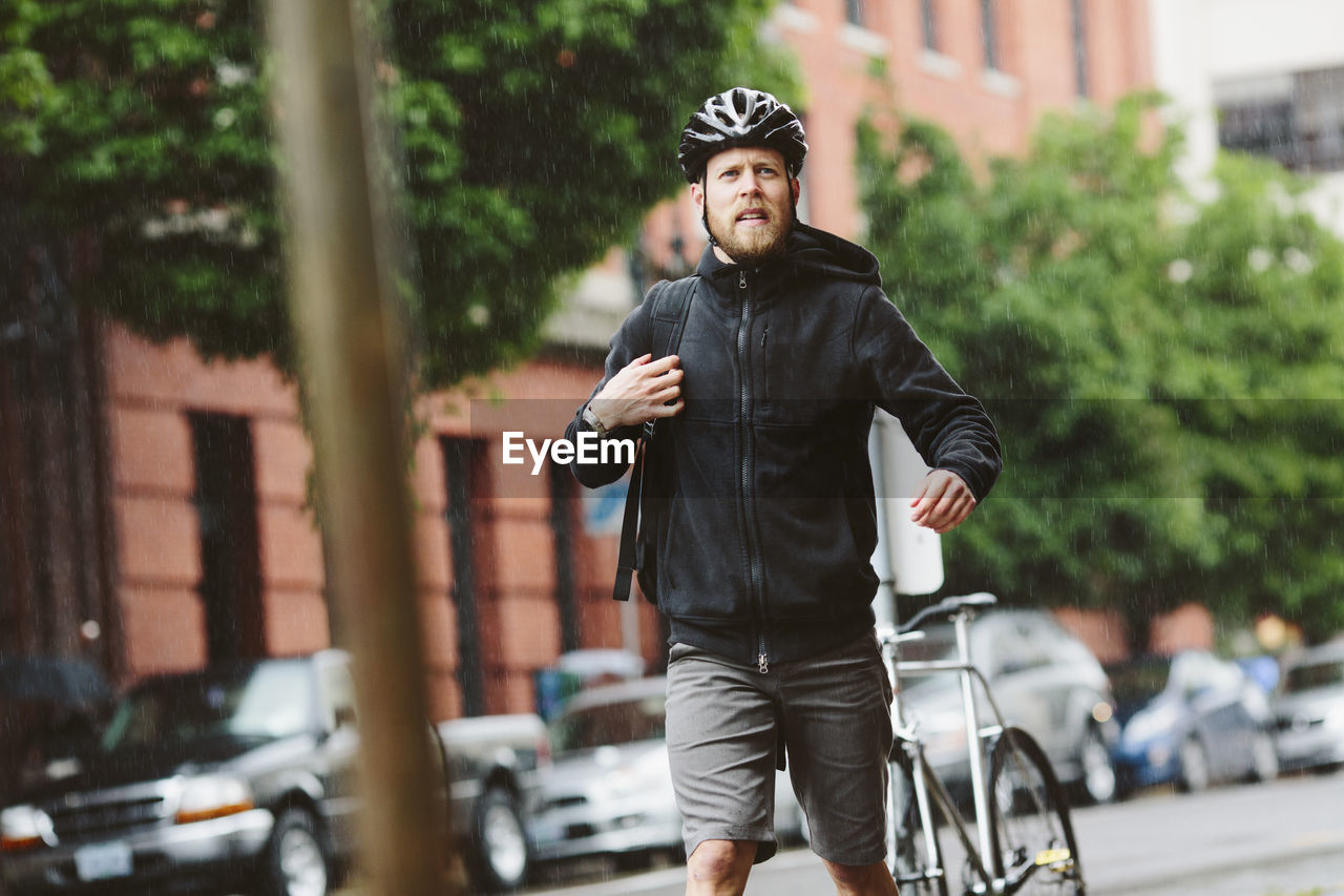 Male commuter looking away while walking in city during rainy season