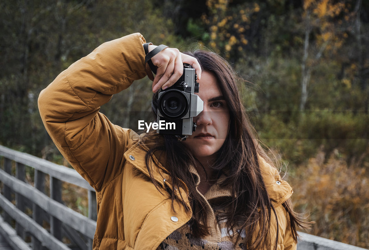 Portrait of young woman taking photos of beautiful autumn nature with a vintage film camera