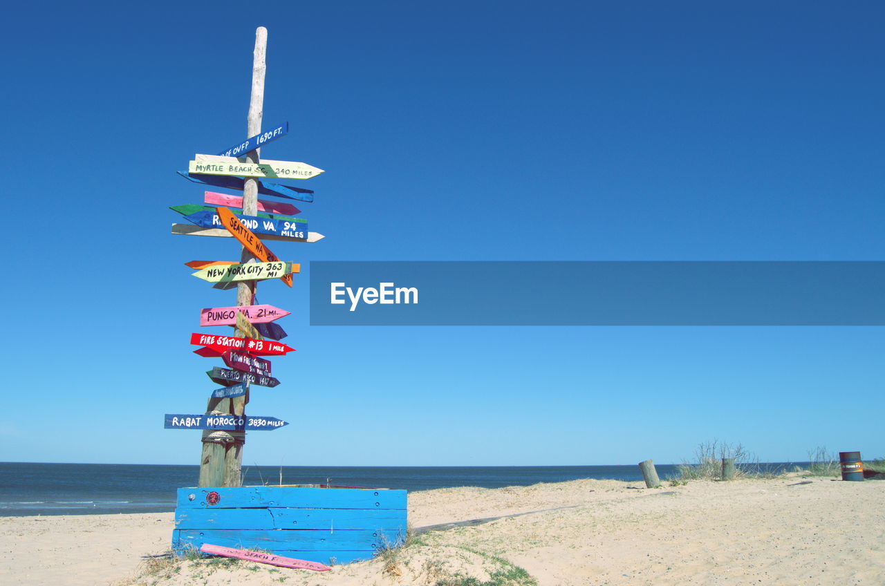 Information sign at beach against clear blue sky