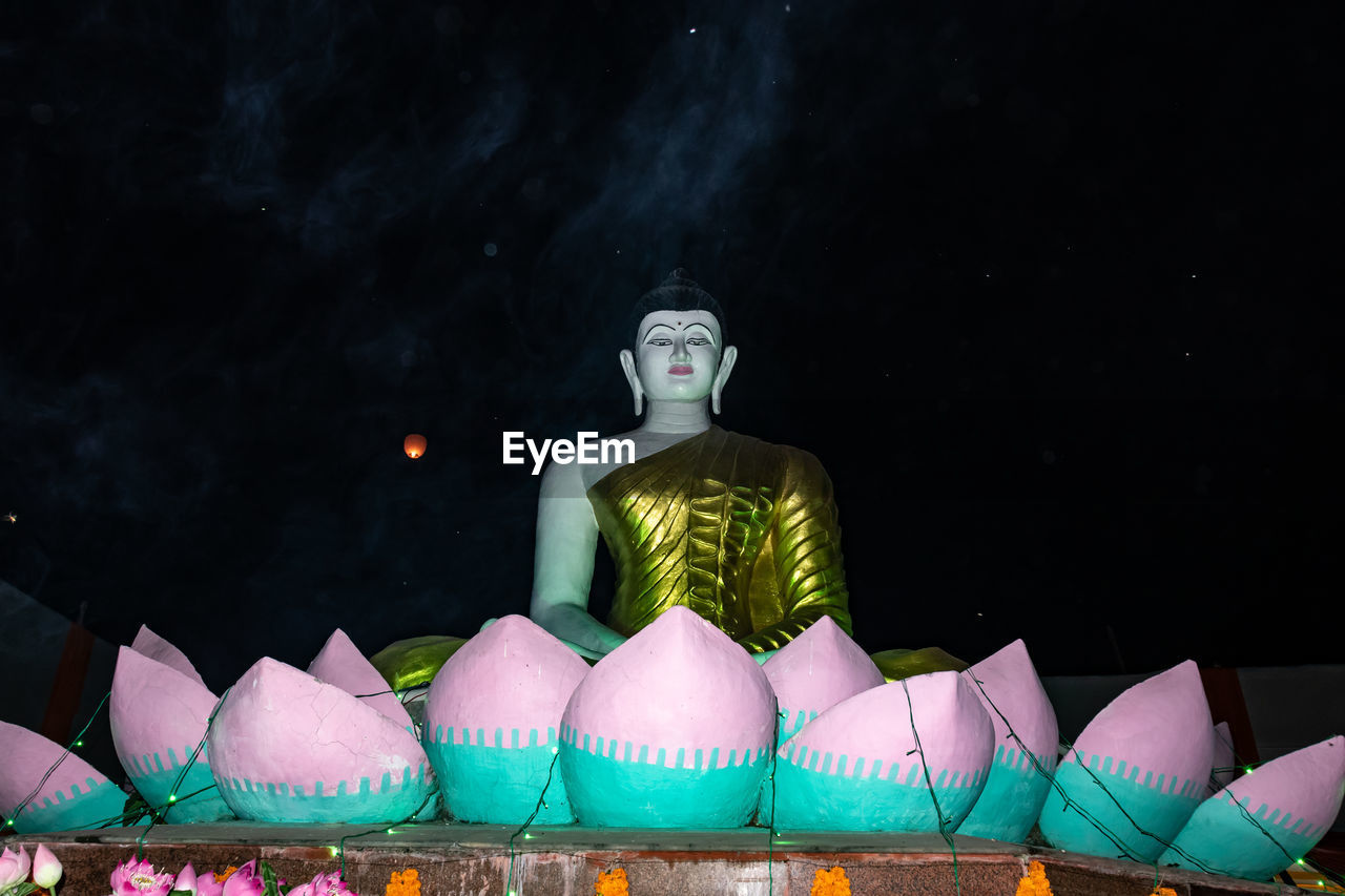 STATUE AGAINST ILLUMINATED TEMPLE AT NIGHT