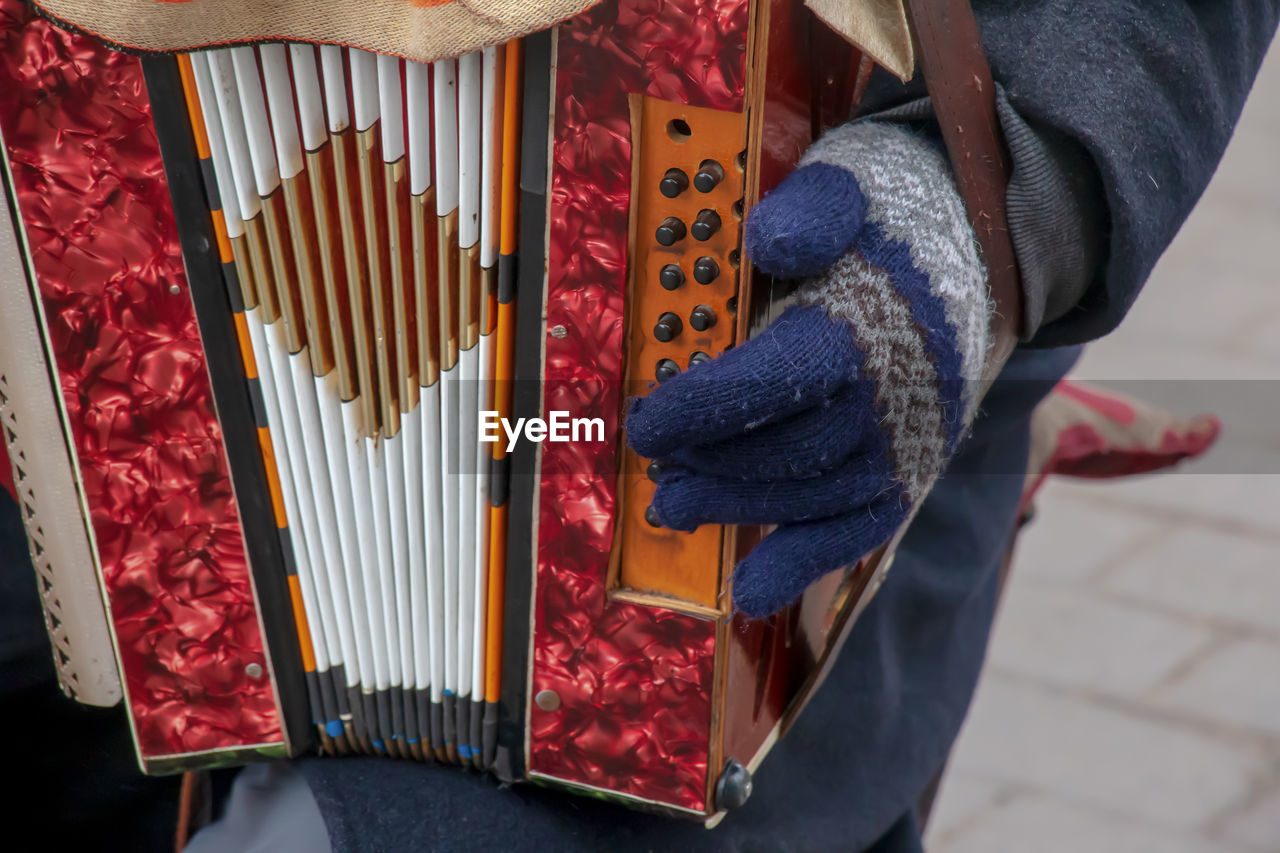 Close-up of a man's hand playing button accordion outdoors in winter.
