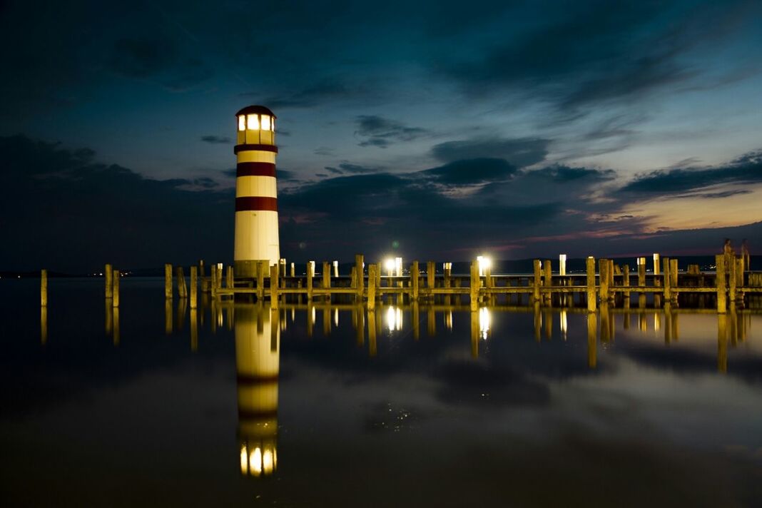 Reflection of lighthouse and jetty in calm sea at night