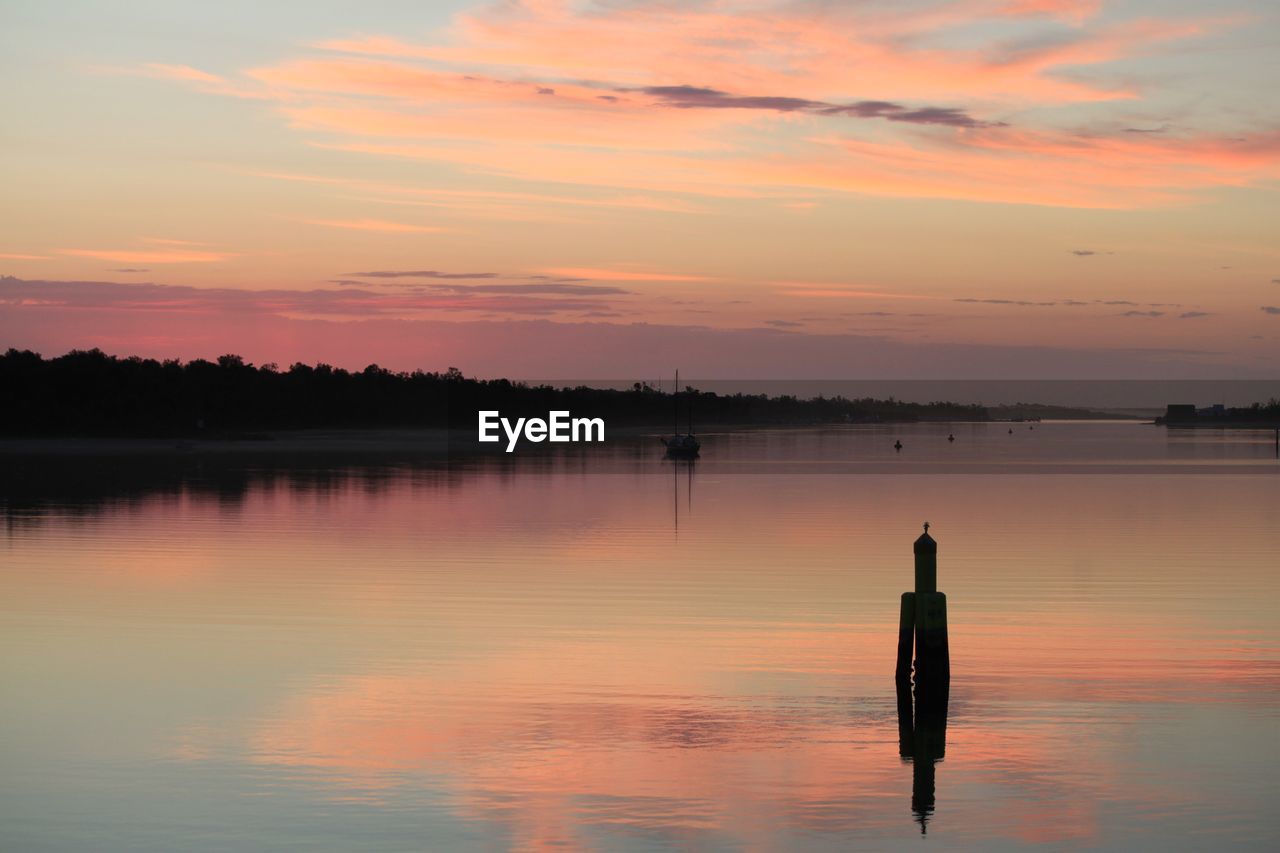 Silhouette wooden posts in lake against sky during sunset