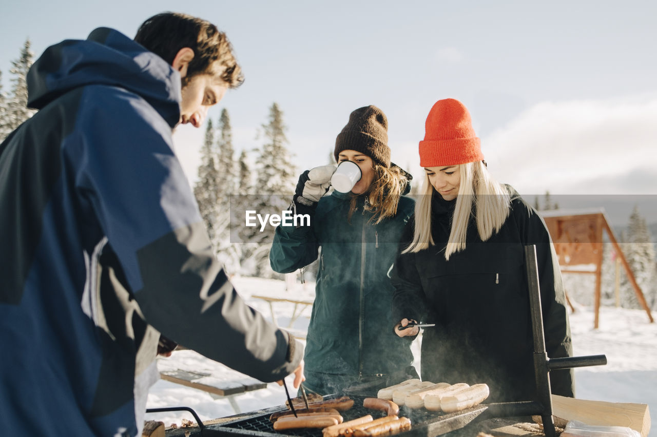 Man preparing sausages while female friends standing at ski resort