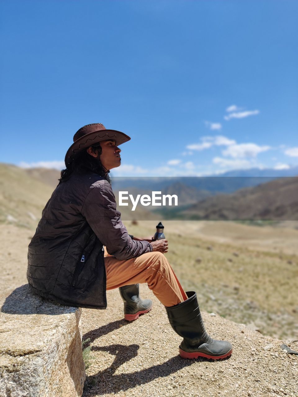 Side view of man sitting on land against sky