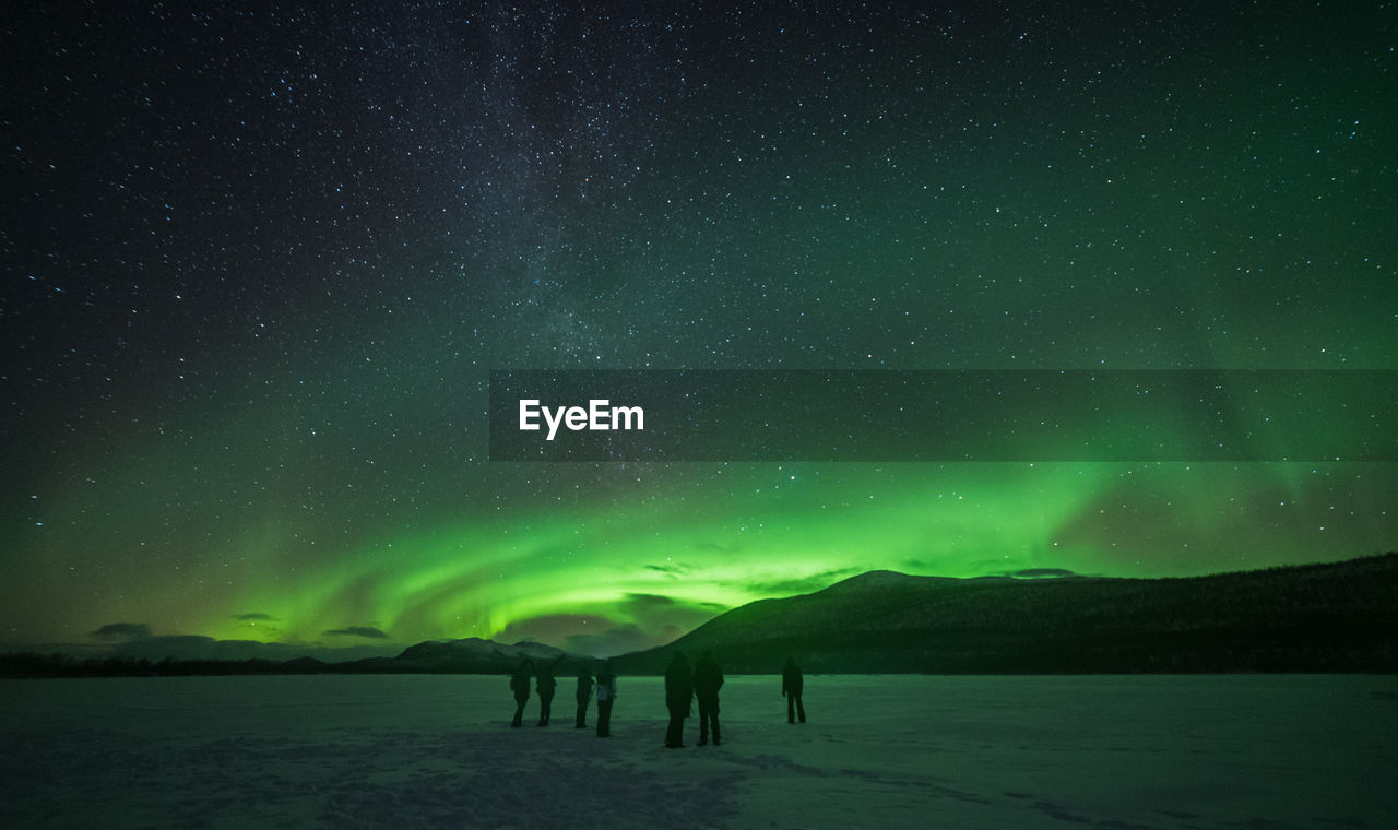 Silhouette people on land with aurora borealis in sky at night