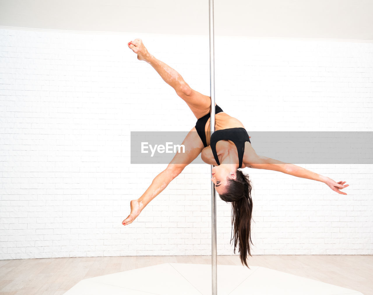 Woman doing pole dance against brick wall