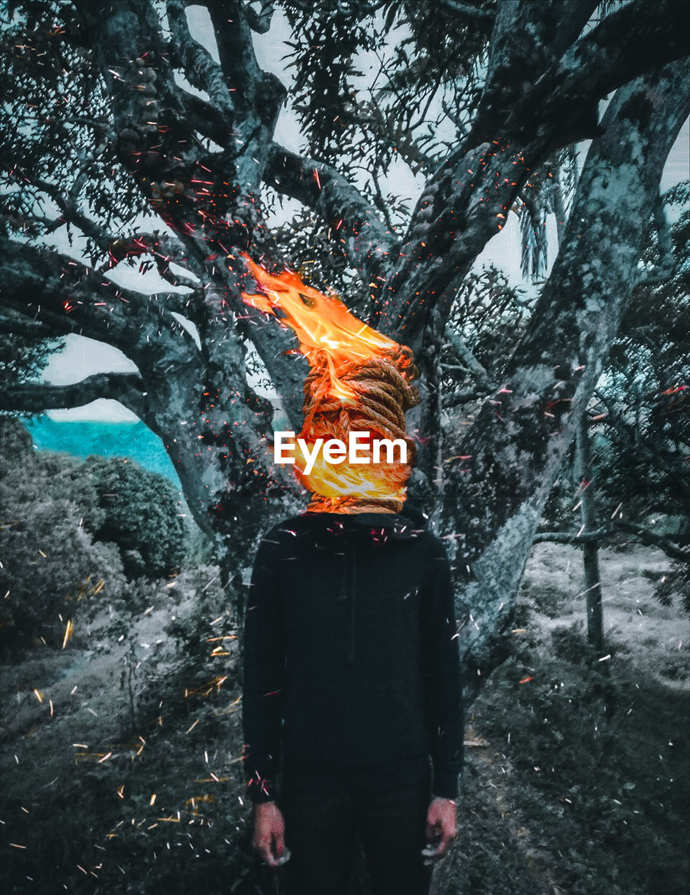 Man with burning head against tree on field