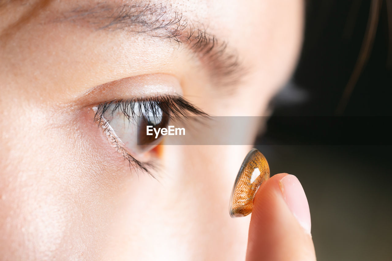 Close-up of woman inserting contact lens in an eye