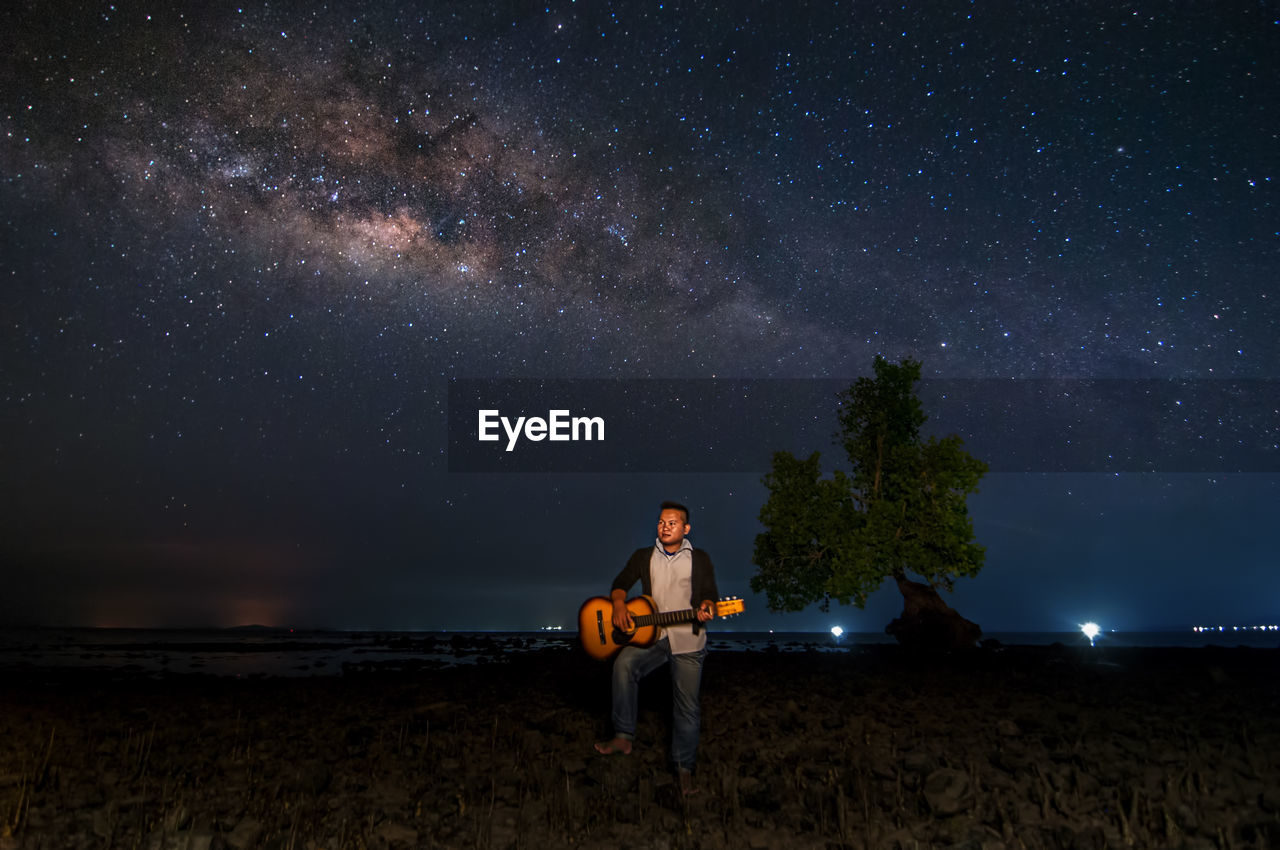 Man playing guitar while standing on land against sky at night