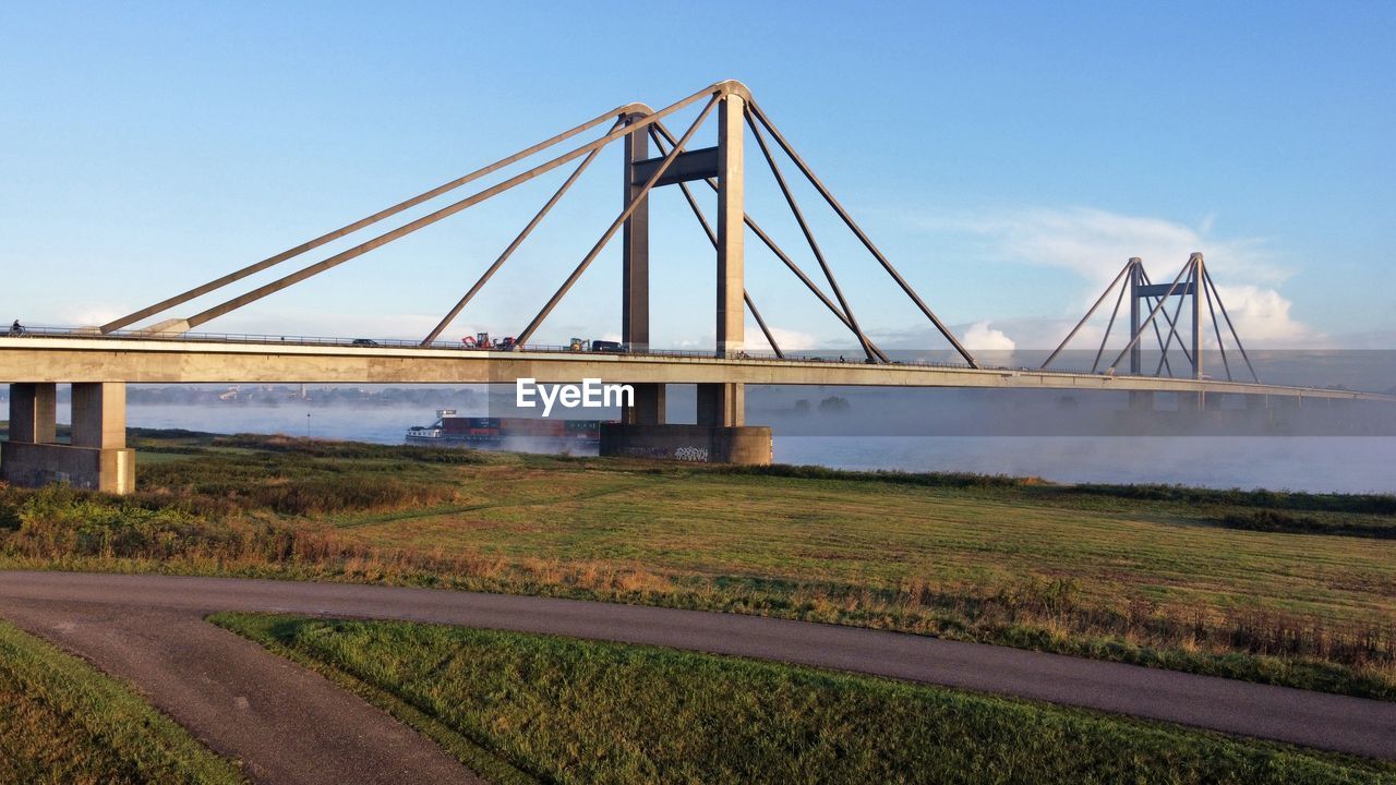 transportation, architecture, bridge, sky, built structure, cable-stayed bridge, water, nature, travel destinations, road, landscape, city, travel, suspension bridge, no people, environment, blue, tourism, scenics - nature, clear sky, outdoors, highway, land, beauty in nature, day, sea, building exterior, landmark, street, urban skyline, cloud, horizon, cityscape, tranquility, copy space, mode of transportation, tranquil scene, sunny, grass, sunlight, building, plant