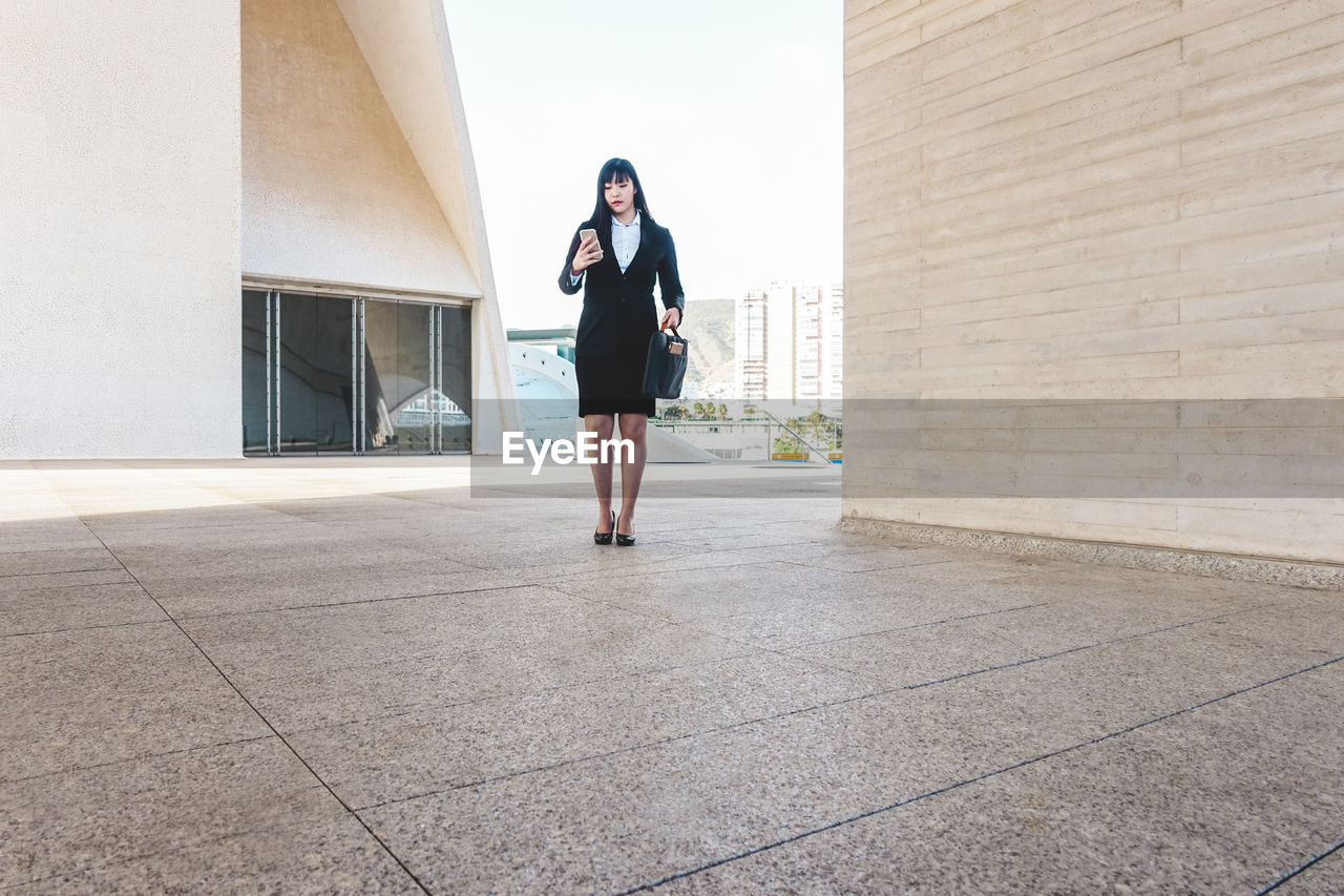 Full length of young woman standing against building