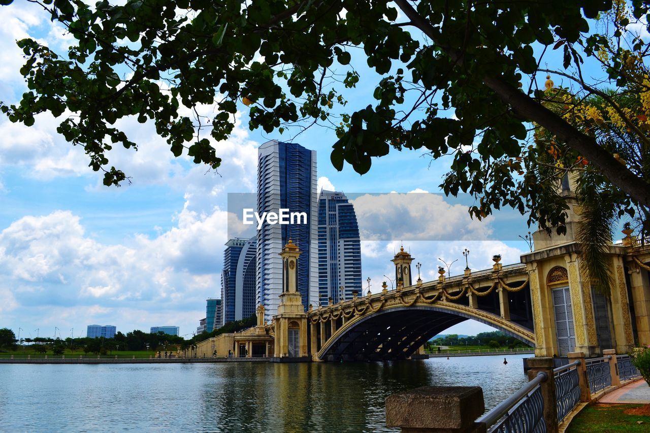 Arch bridge over river by buildings against sky