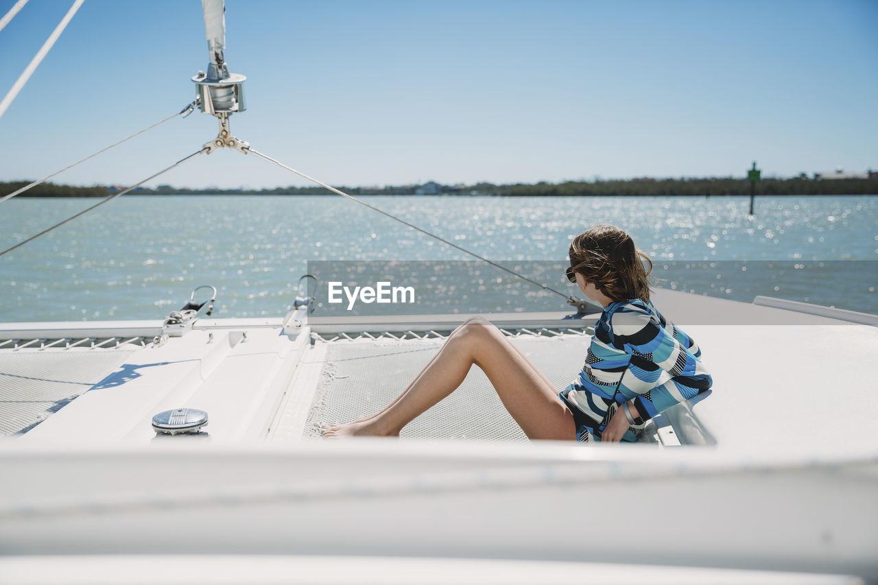 Side view of girl sitting in boat on sea against clear sky during sunny day