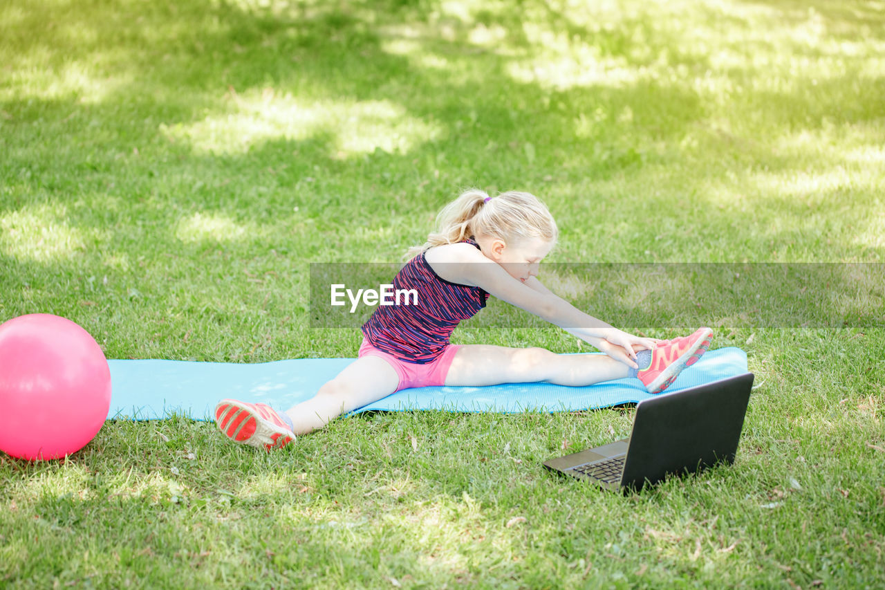 Caucasian girl child doing sport workout outdoor online. video yoga stretching on internet. 