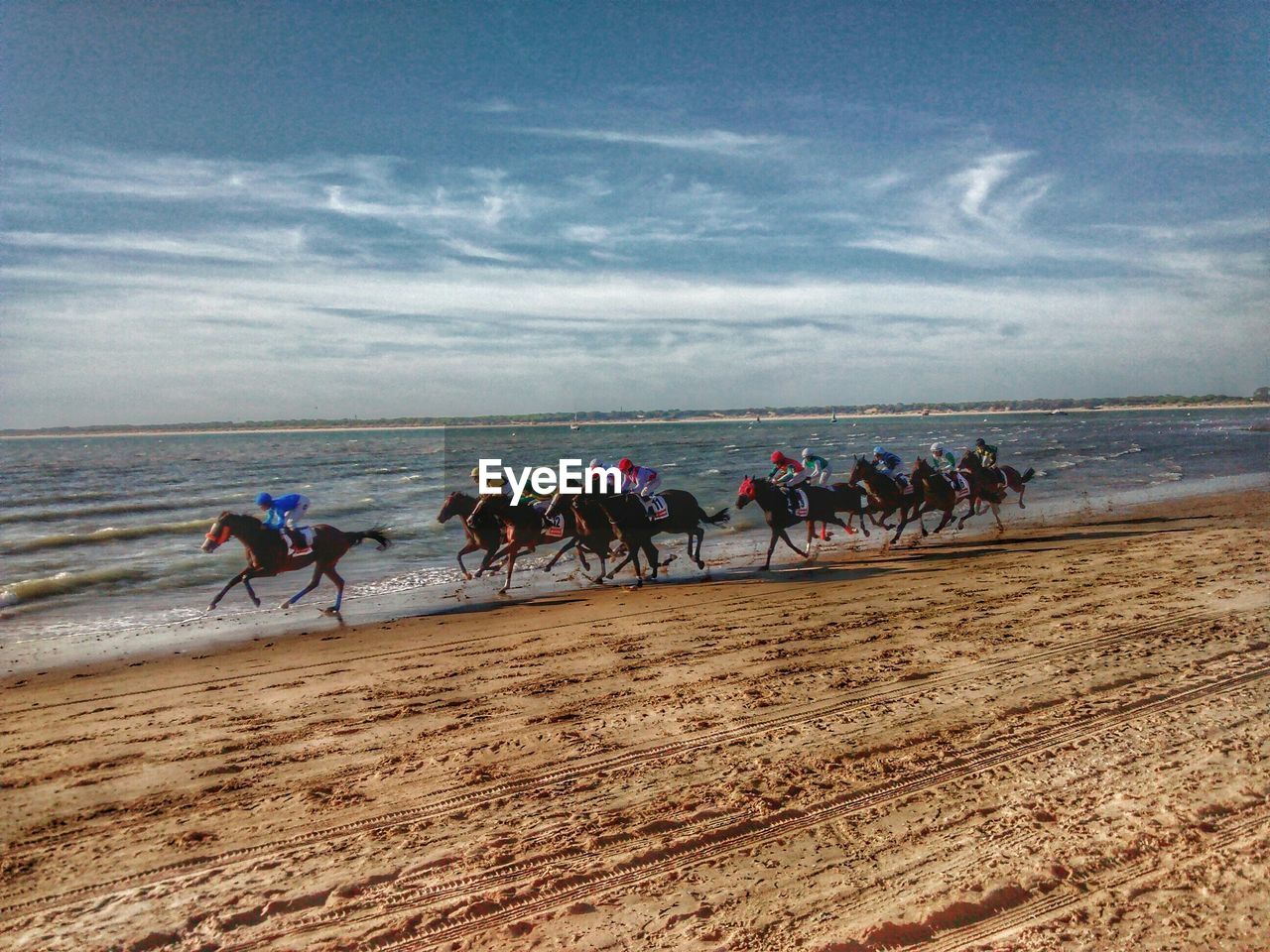 Horse racing on beach against cloudy sky