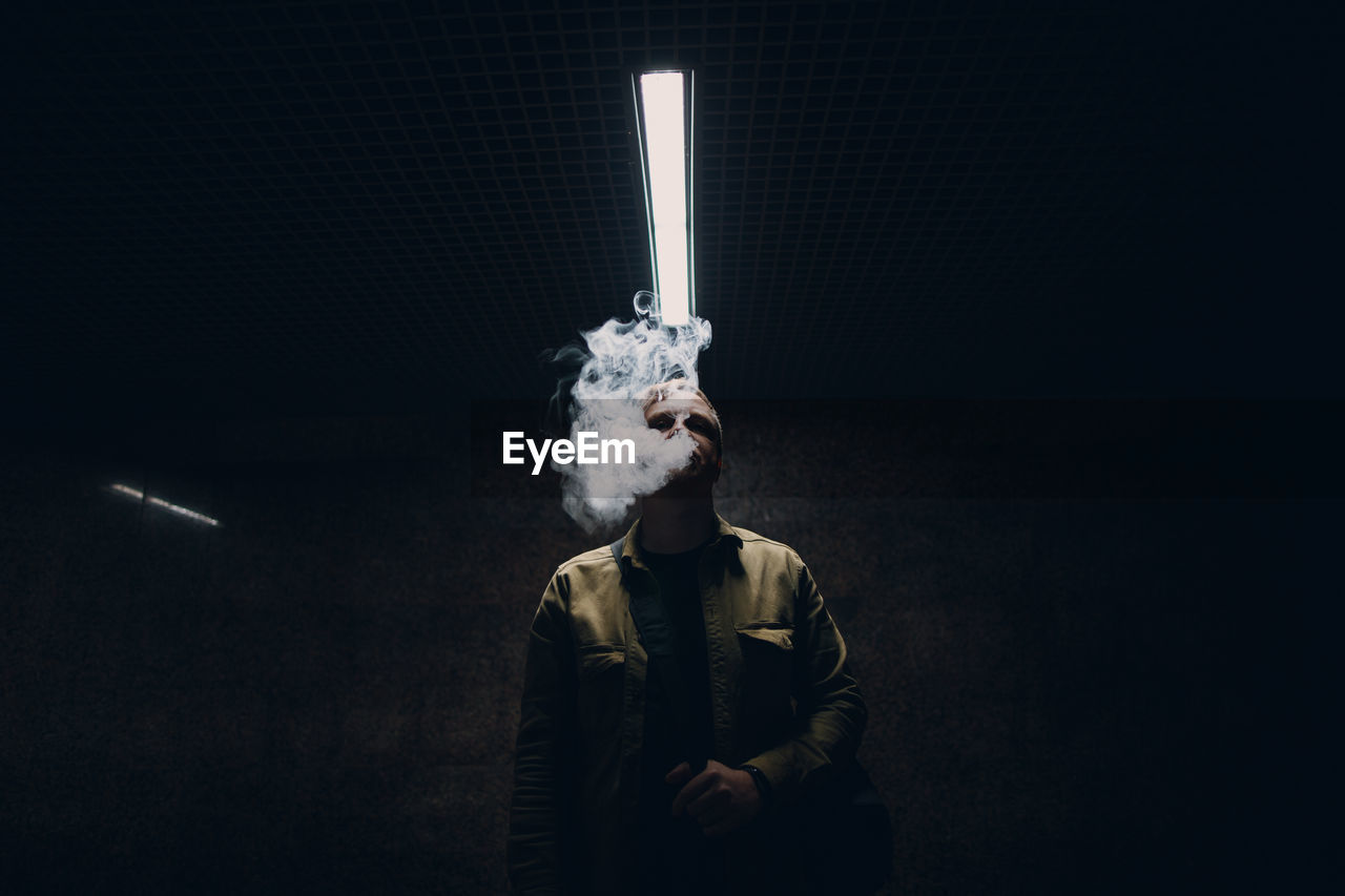 Portrait of man smoking cigarette against black background