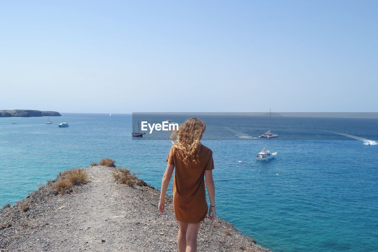 Rear view of woman walking at beach against clear sky