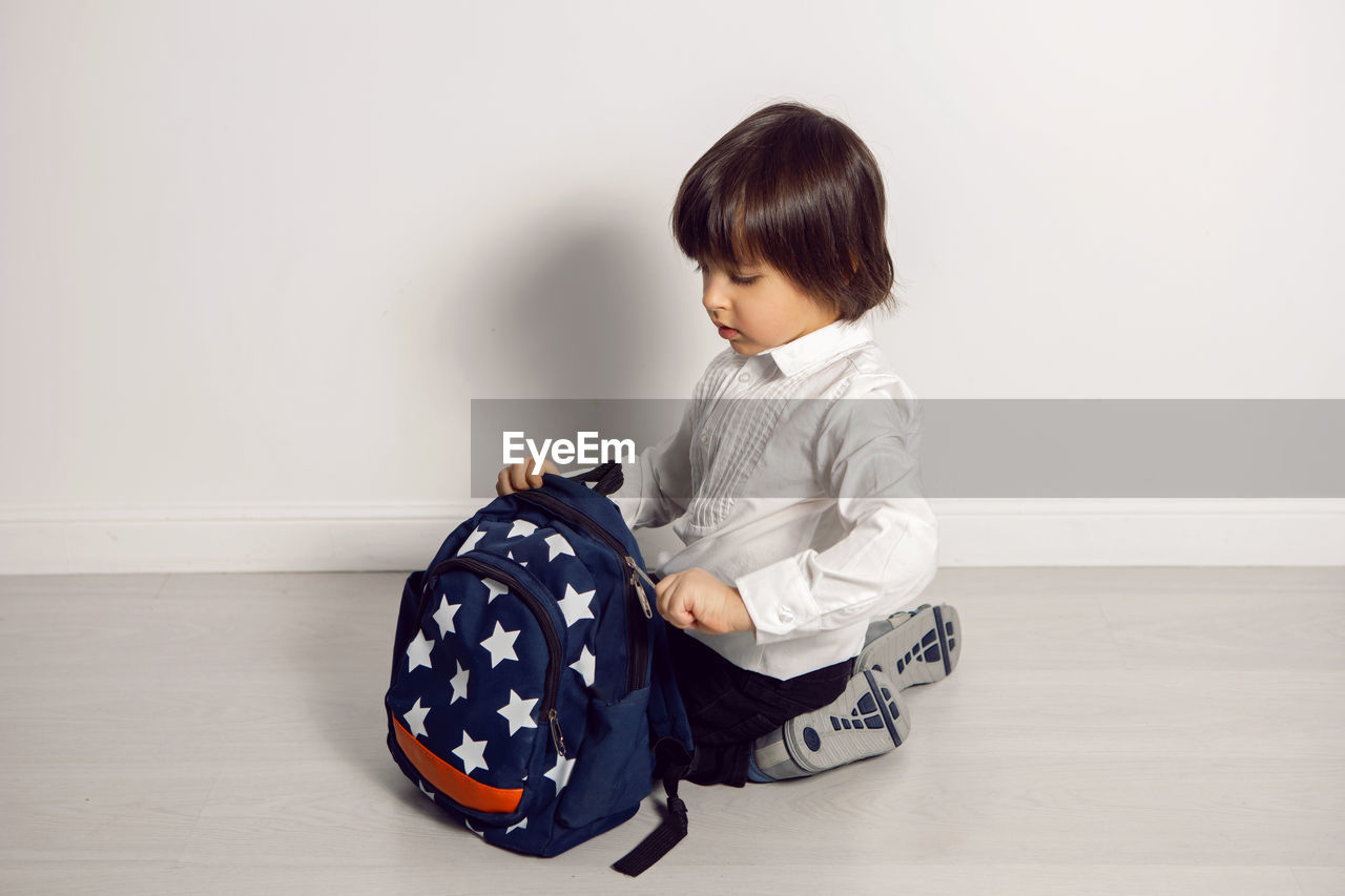 Child boy with a book textbook and backpack sit on a white background