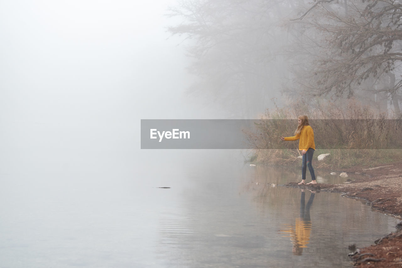  side of view of young girl, skipping stones on a foggy lake 