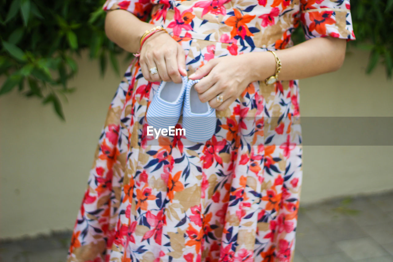 Midsection of pregnant woman holding baby booties on abdomen