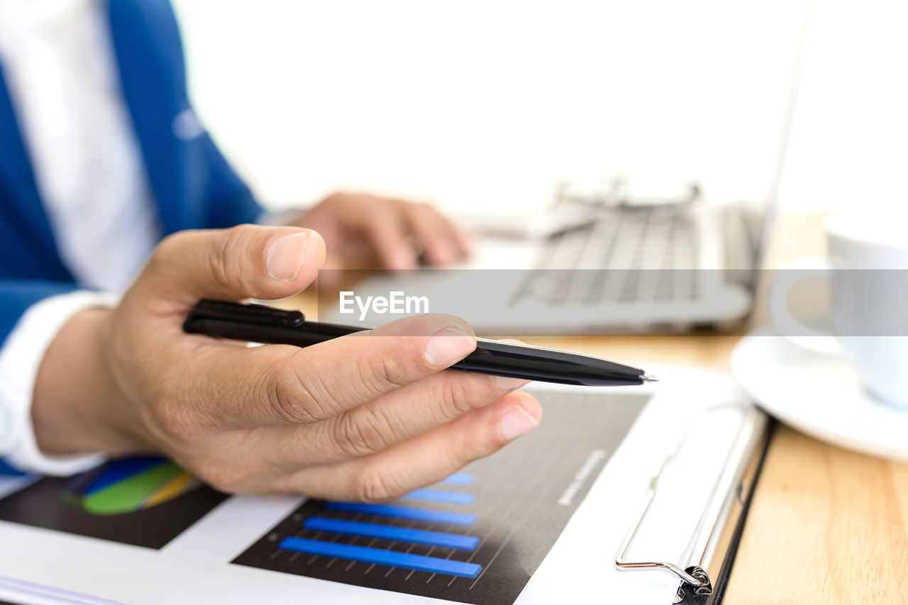 CROPPED IMAGE OF MAN USING MOBILE PHONE ON TABLE