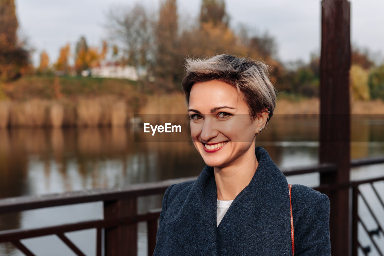 A woman smiles broadly near the river in autumn