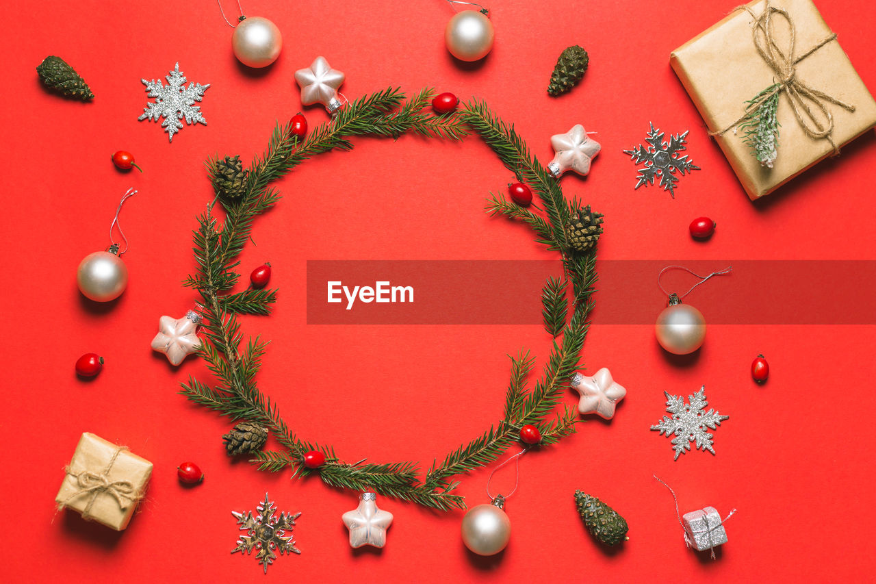Wreath of fir, pine cones, rowan berries, anise, balls and gift boxes on red background