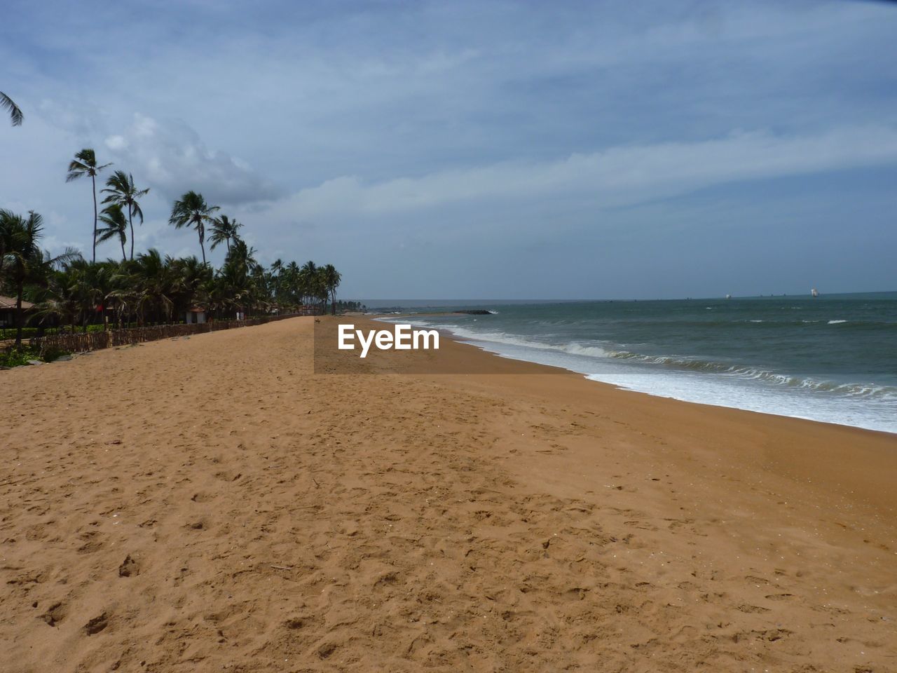 Scenic view of beach against cloudy sky during sunny day